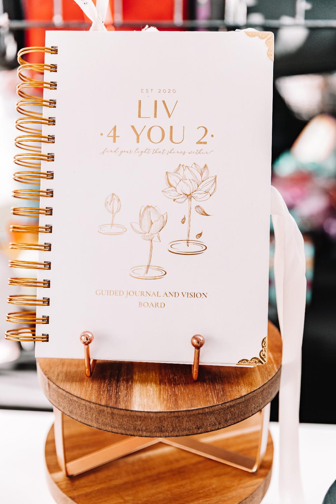 Liv 4 You 2 Cream and gold hardcover manifestation guided journal and vision board on brown wooden pedestal