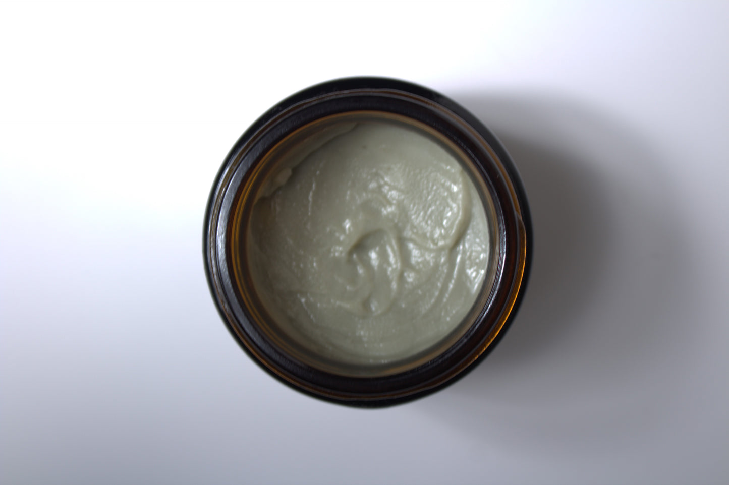 Green facial cleansing balm in brown, glass jar, on white surface