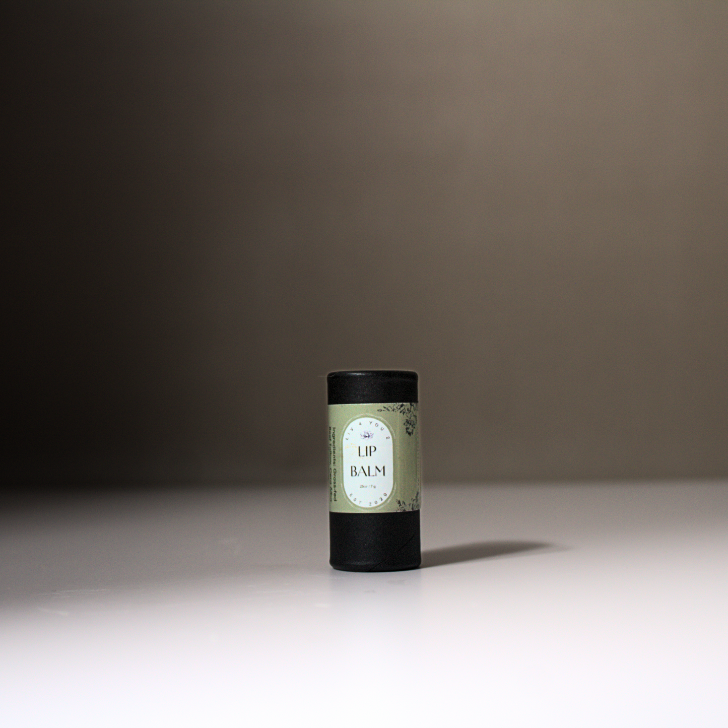 Black carboard lip balm tube with a green label and black writing.