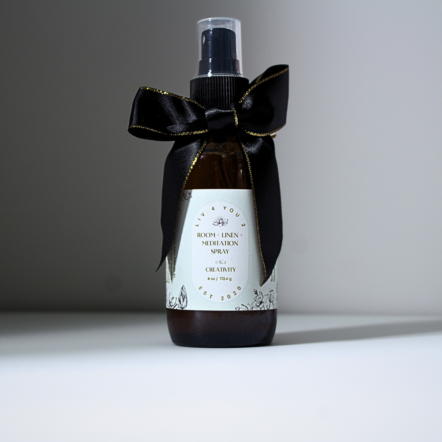 Room spray in brown glass bottle with black and gold bow with white label and black writing for Liv 4 You 2